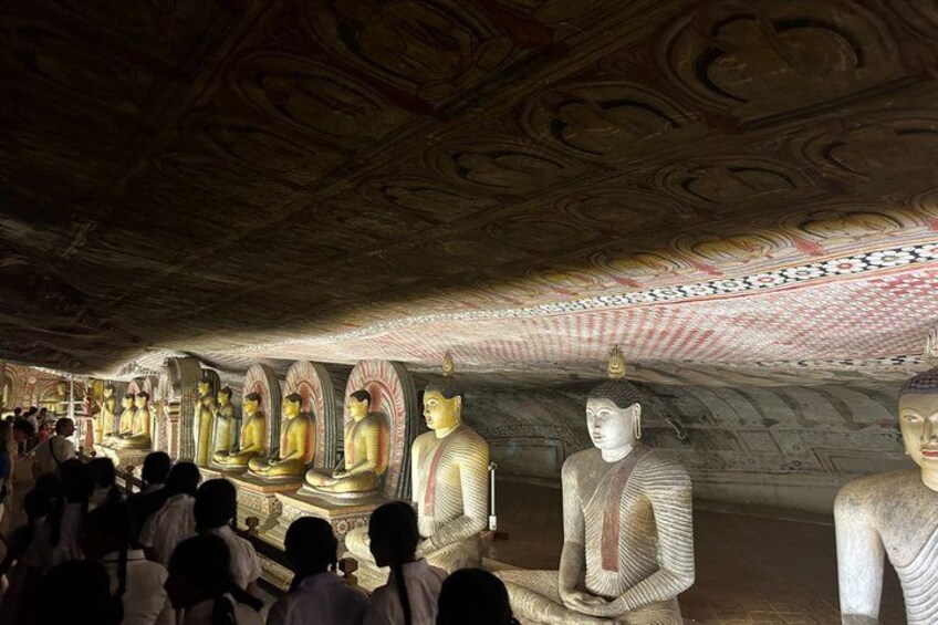 A row of large Buddha statues in a cave with intricate ceiling carvings. 3