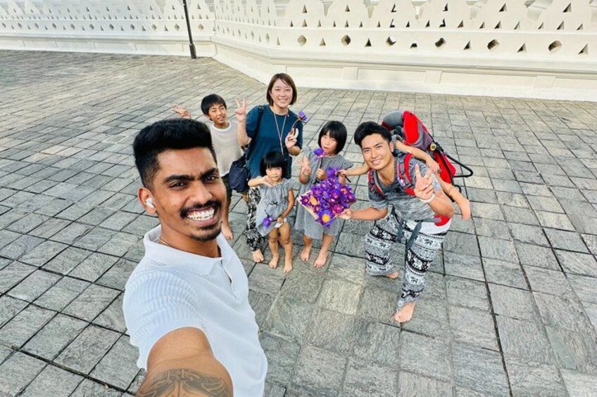 A group of people posing for a selfie on a paved area with a patterned wall in the background. 5