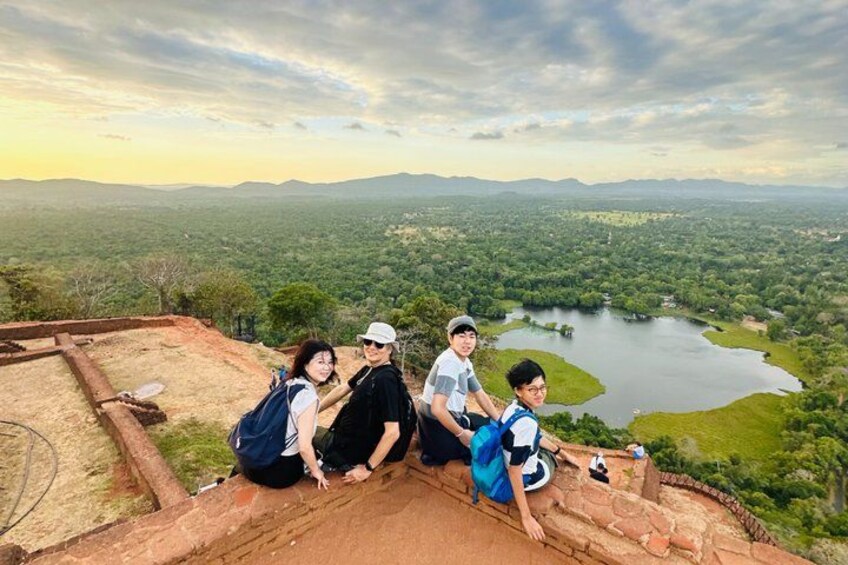 A group of people sitting on a stone platform overlooking a lake and forested landscape. 2
