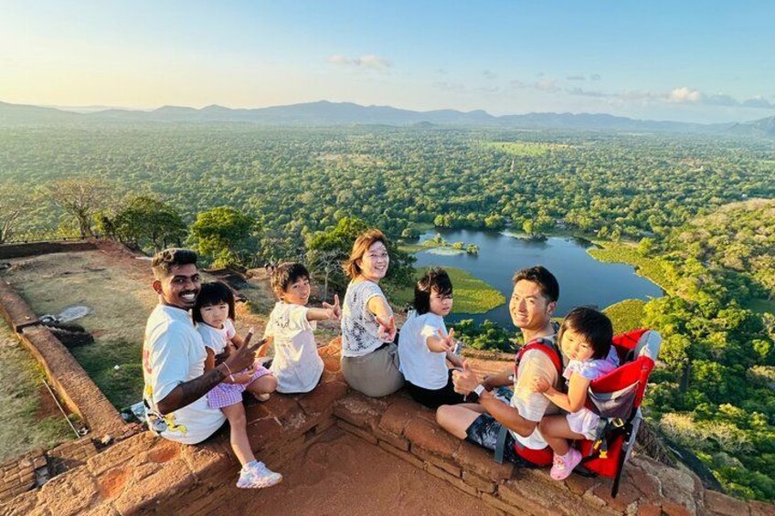 A group of people sitting on a ledge overlooking a vast landscape with a river and distant mountains. 1
