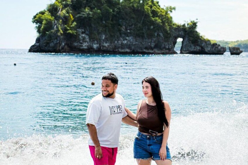 A couple standing by the sea with a rocky island in the background. 4