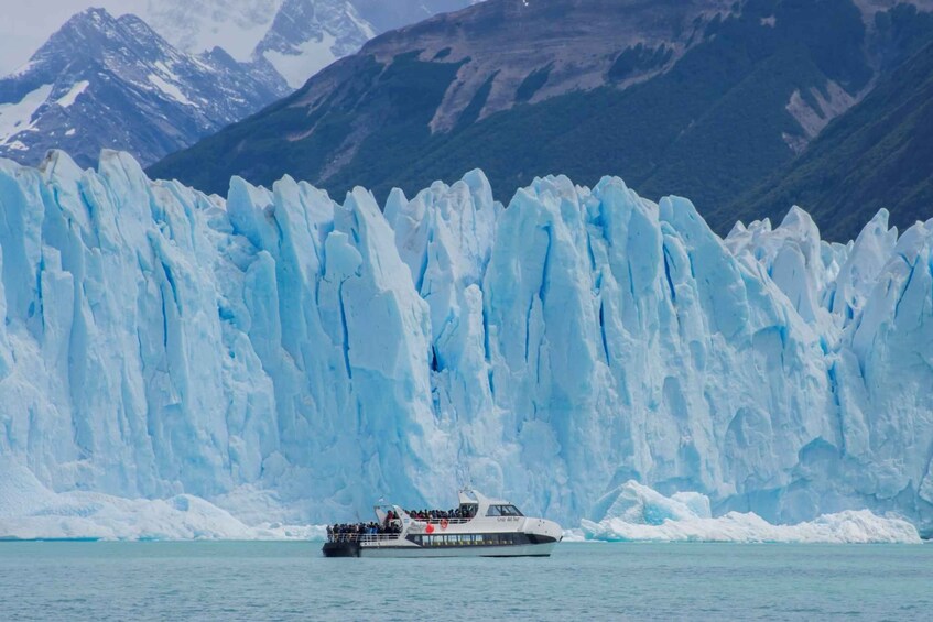 A cruise ship with passengers in front of a large glacier. 1