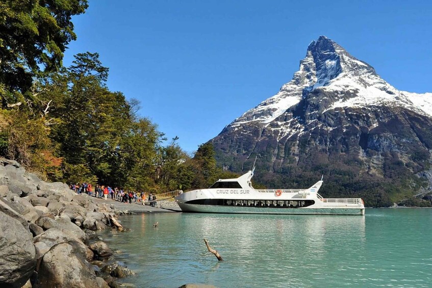 A boat named 'CRUZ DEL SUR' docked at a rocky shore with a snow-capped mountain in the background. 3