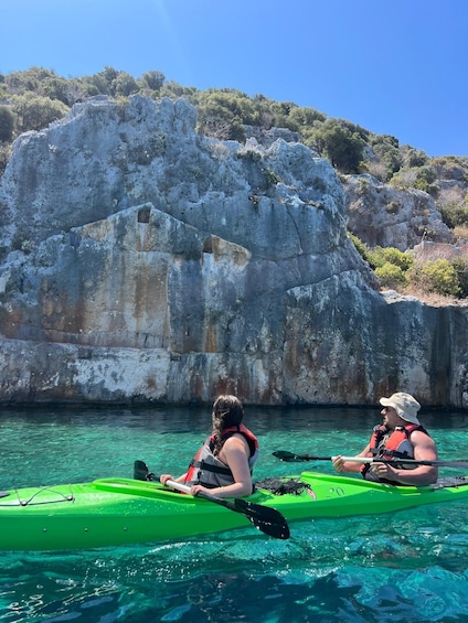 Två personer paddlar kajak på en solig dag med branta klippor i bakgrunden. 4