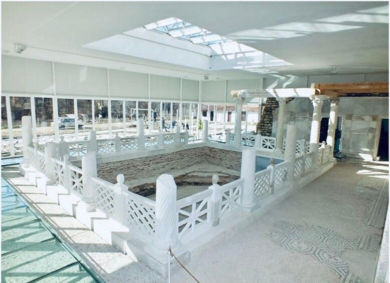 An archaeological site with a white fence, a glass roof, and a stone structure. 4