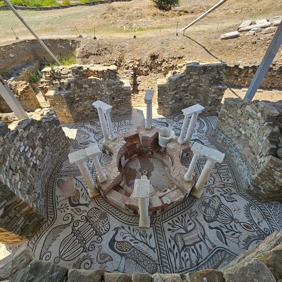 An ancient mosaic with a central circular design surrounded by stone columns. 3