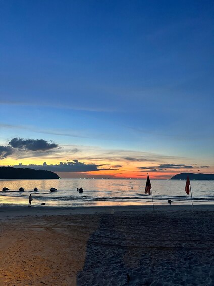 A beach at sunset with boats and flags. 4