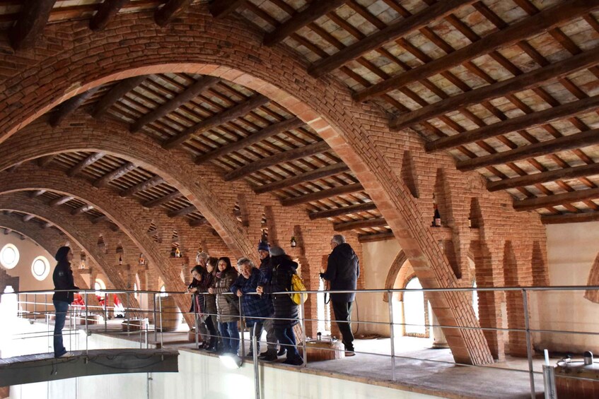 A group of people standing on a balcony with a brick ceiling and arches. 4