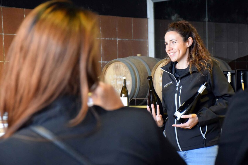 A person holding a wine bottle in a setting with barrels in the background. 3