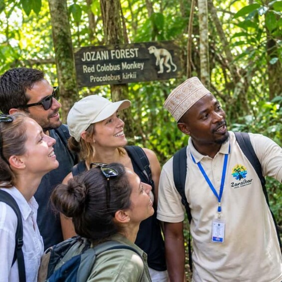 A group of people in a forested area with a sign indicating the presence of a Red Colobus Monkey. 3