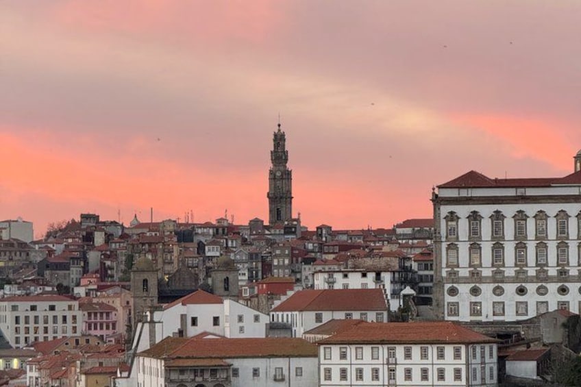 A cityscape with a prominent tower and a mix of historical and modern buildings under a pink sky. 2