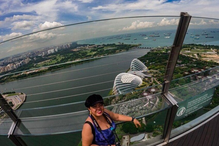 A person on a glass bridge with a view of a river, buildings, and boats. 2