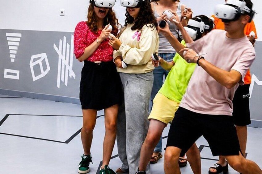 People wearing VR headsets in a room with a white floor and a gray wall with white geometric shapes. 3
