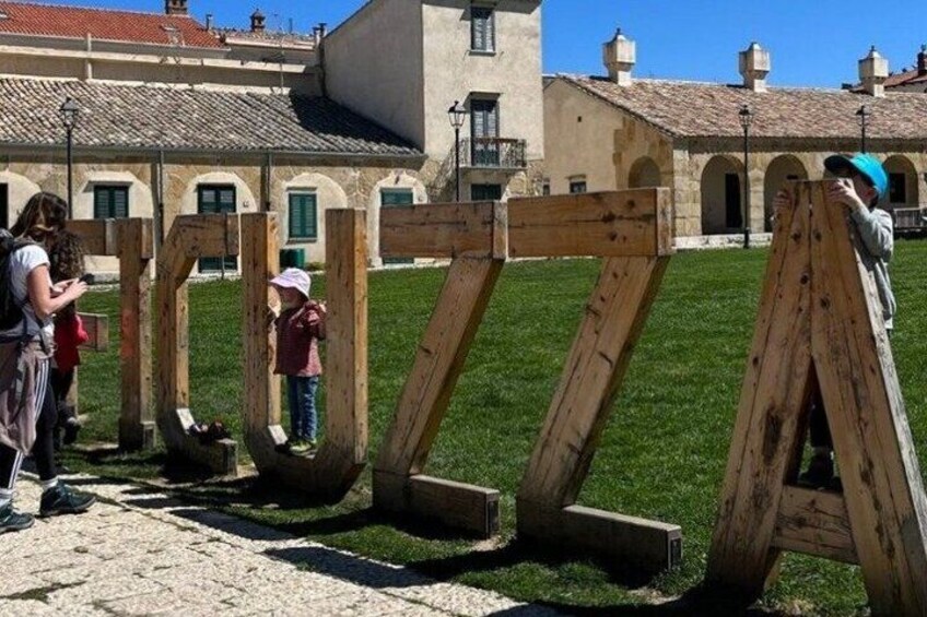 Wooden structures resembling letters, a grassy area, and a building with arched windows in the background. 2