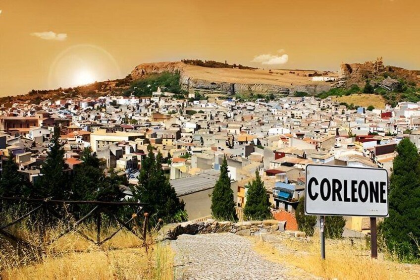A town with a sign reading 'CORLEONE' amidst a landscape with buildings and a hill in the background. 1