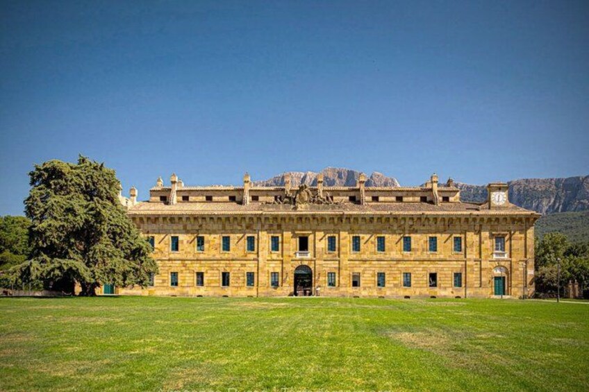 A large, historic building with a symmetrical facade, a central entrance, and a mountainous backdrop. 4
