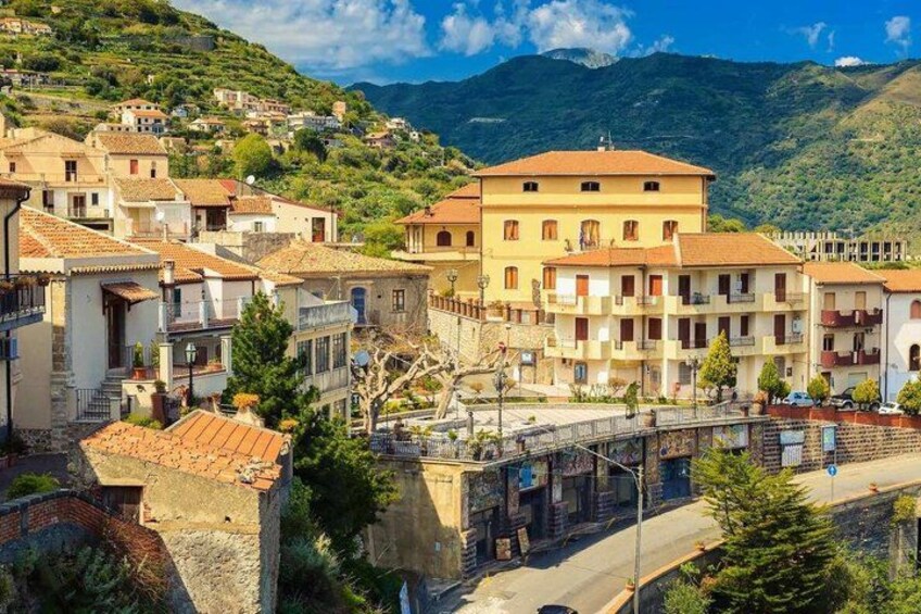A hillside town with terracotta-roofed buildings, a bridge, and a mountainous backdrop. 5