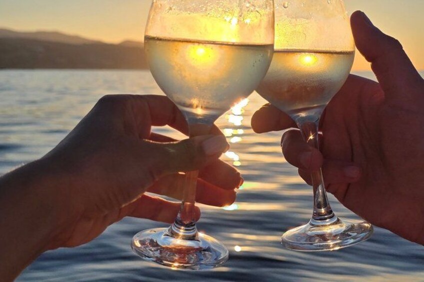 Dos manos sosteniendo copas de vino con un atardecer de fondo. 2