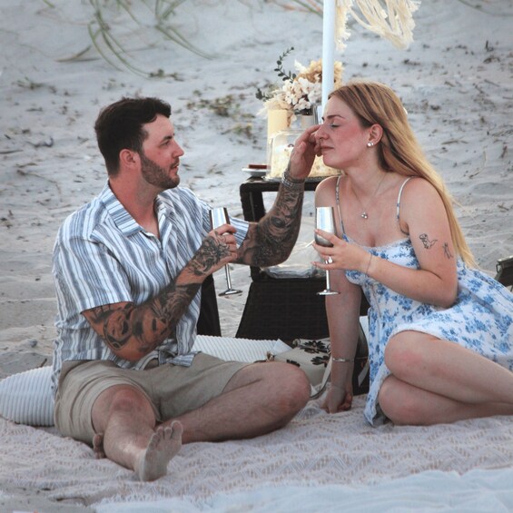 Two people sitting on a beach blanket, holding wine glasses. 3