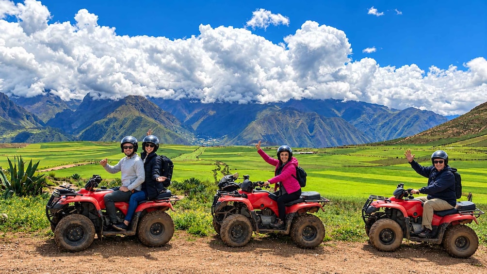 Drei Personen fahren mit Quads durch eine ländliche Landschaft, im Hintergrund Berge. 5