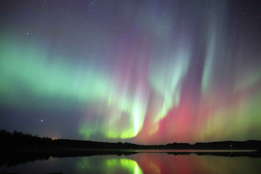 Revontulet peittyvät tyynen järven ylle, ja järven rannalla kohoaa metsä. 1