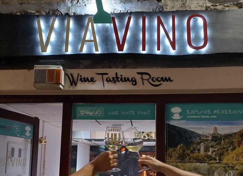 A sign for 'VIA VINO Wine Tasting Room' with a wine glass logo and a scenic background. 4