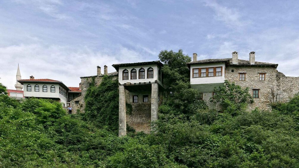 A historic stone building with arched windows and a tower, surrounded by lush greenery. 3