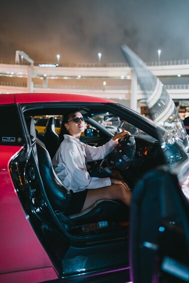 Een persoon zit in een rode cabriolet met een openstaande deur, en houdt een autosleutel vast. 4