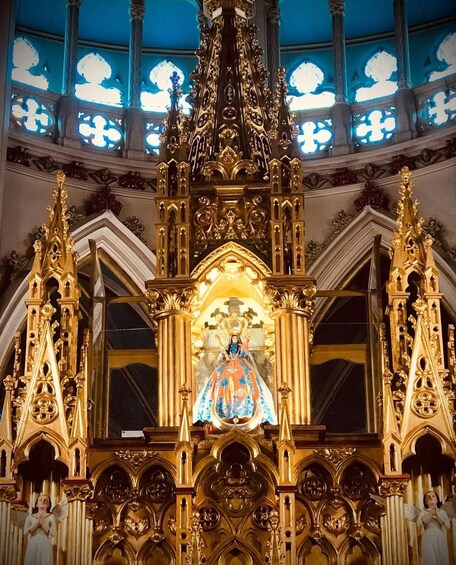 An ornate church interior with a central statue, intricate gold detailing, and stained glass windows. 4