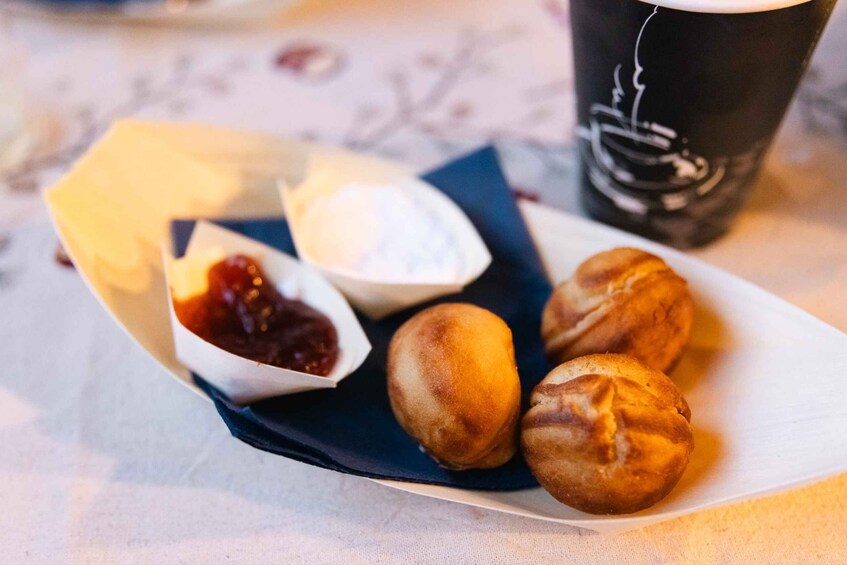 A plate of three round pastries, a small bowl of jam, and a cup of coffee on a table. 5