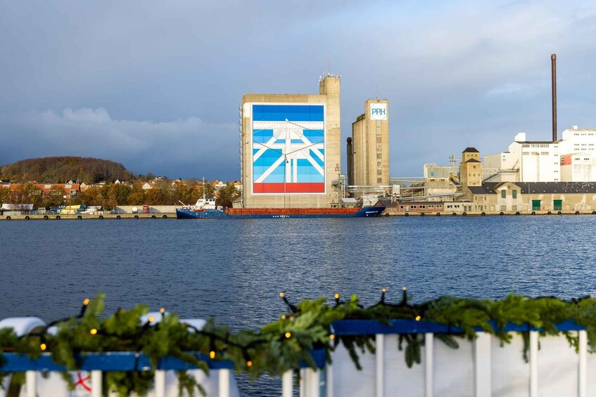 A large industrial building with a distinctive blue and white logo, a river with boats, and a cityscape in the background. 4