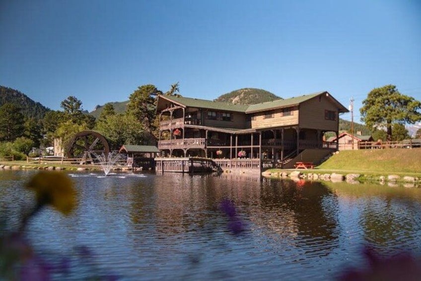 A large wooden building with a water wheel, surrounded by a lake and hills. 1