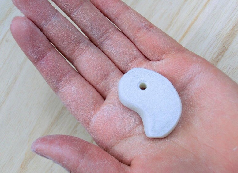 A hand holding a white ceramic object with a hole. 2