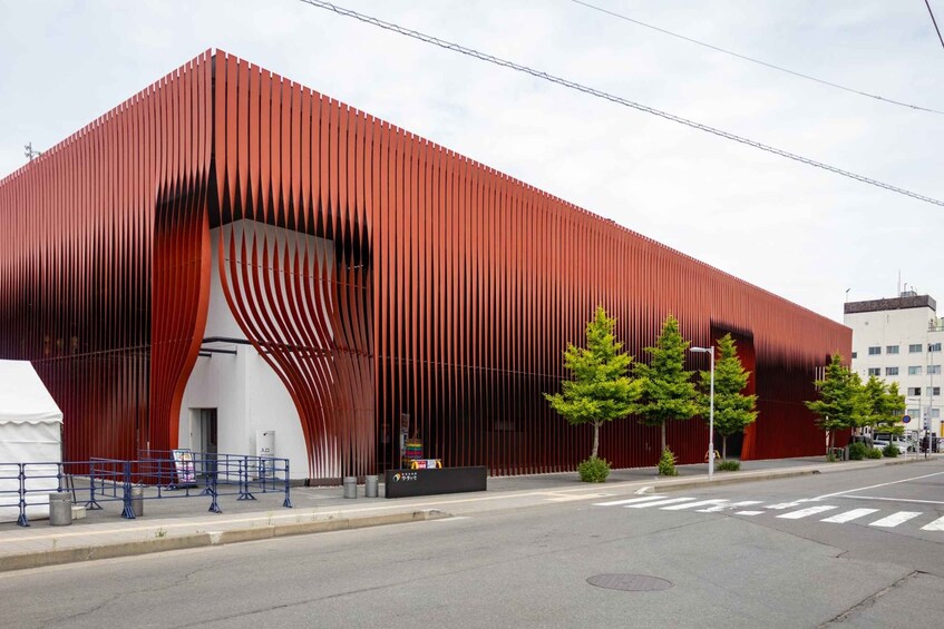A modern red building with vertical slats, a white entrance, and a street with a crosswalk. 4