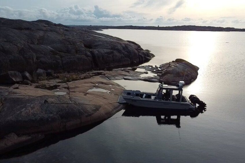 A boat docked on a rocky shoreline with calm water reflecting the sky. 3