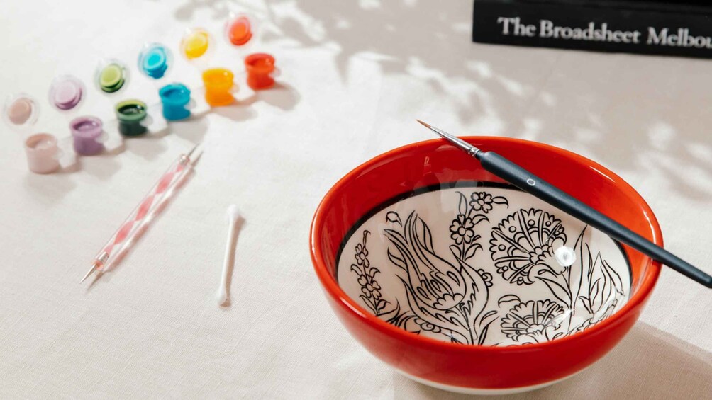 A bowl with a floral design, a paintbrush, and a set of watercolor paints on a table. 3
