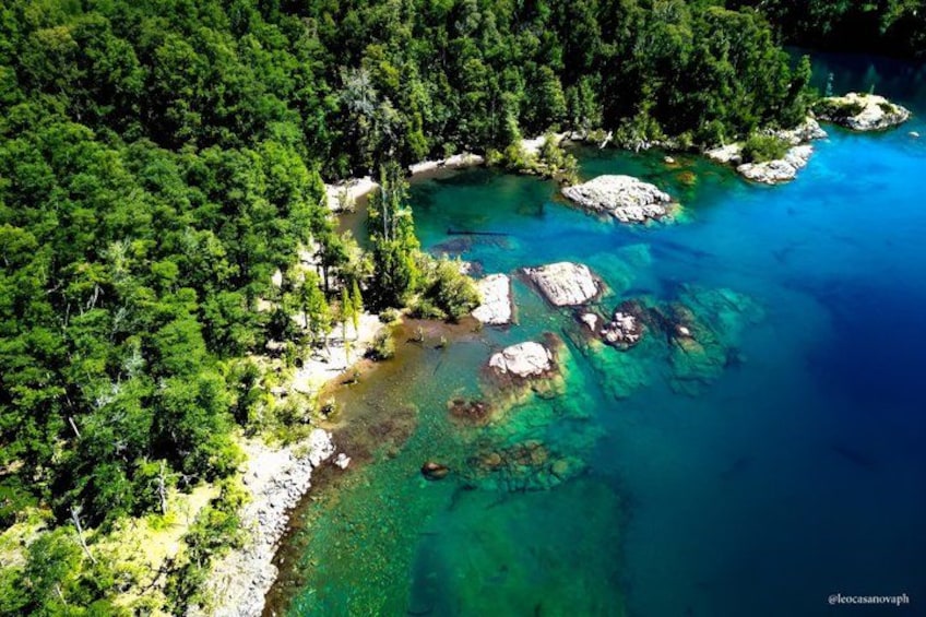A coastal landscape with clear turquoise waters, rocky outcrops, and dense green forest. 2