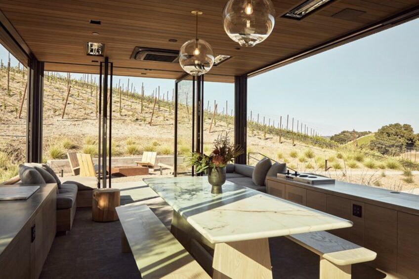 A modern interior with a large glass table, wooden ceiling, and a view of a desert landscape. 5