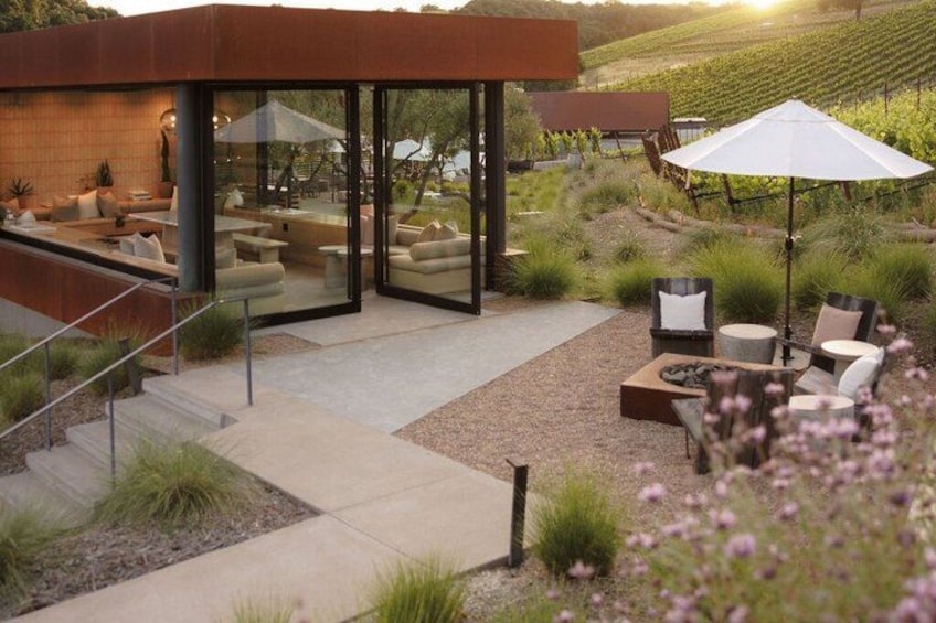 A modern outdoor patio with seating and a glass enclosure, surrounded by a vineyard landscape. 1