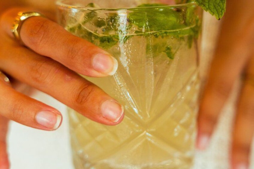 Una mano sosteniendo un vaso con una bebida, hojas de menta y una superficie de vidrio texturizada. 1