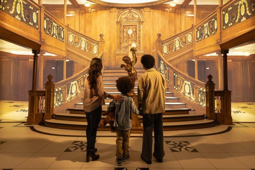 A family standing in a grand, ornately decorated hall with a large staircase. 1