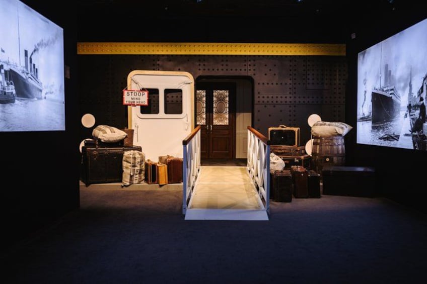 A dimly lit corridor with vintage suitcases and a vintage car, leading to a door with a sign that reads 'STOP YOUR HEAD.' 5