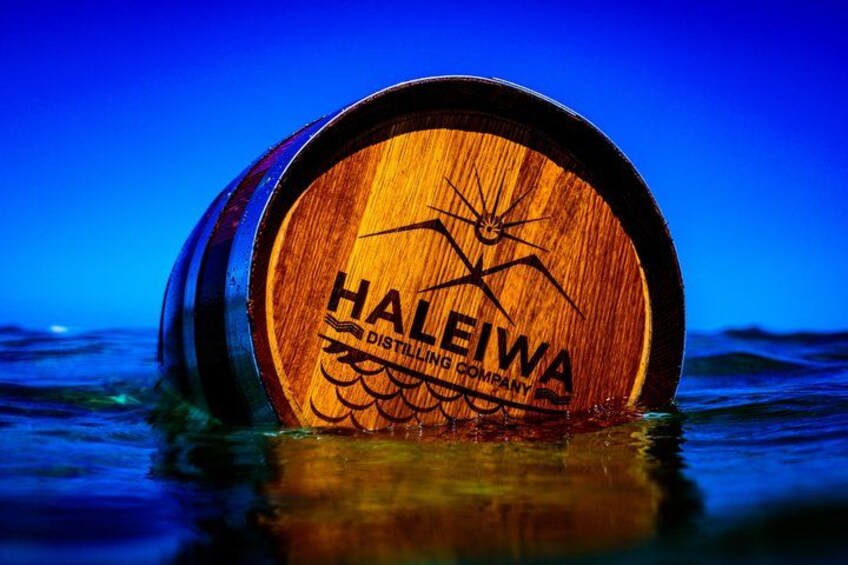 A wooden barrel with 'HALEIWAWA DISTILLING COMPANY' engraved on it, floating in water. 2
