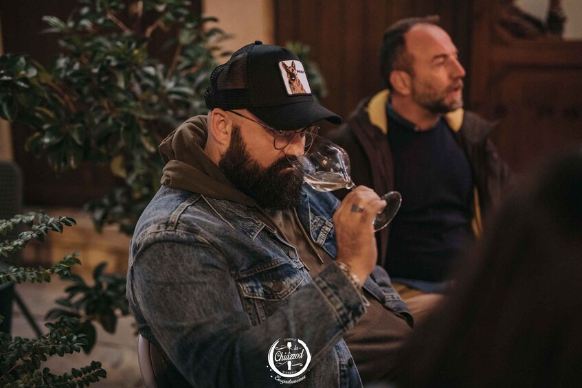 A person wearing a denim jacket and a cap with a logo, holding a glass. 2
