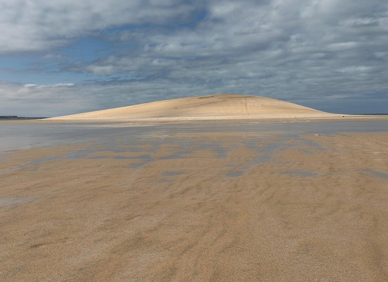 A sandy beach with a large dune in the background under a cloudy sky. 2