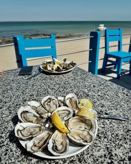 A plate of oysters on a table with a phone and a blue chair in the background. 4
