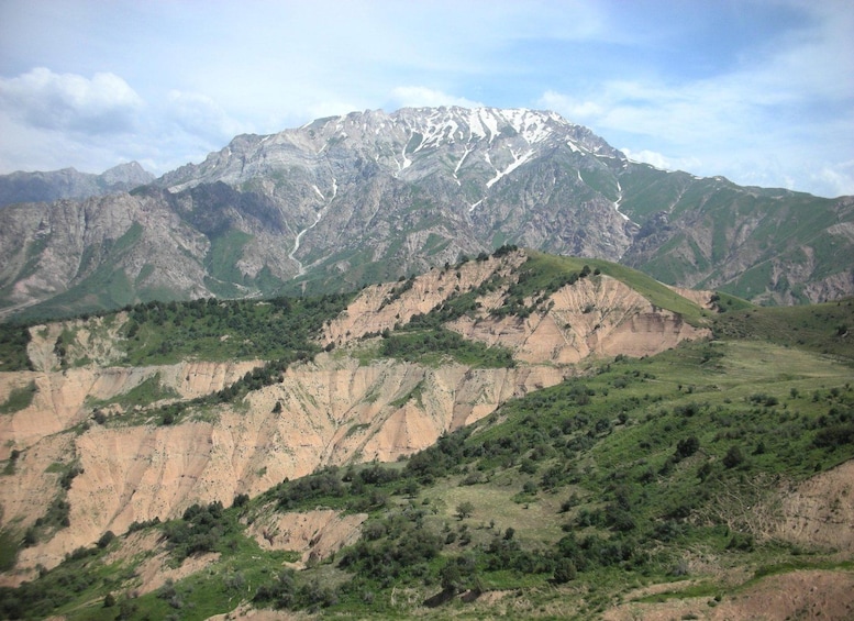 A mountainous landscape with a prominent peak covered in snow, green valleys, and rugged terrain. 3