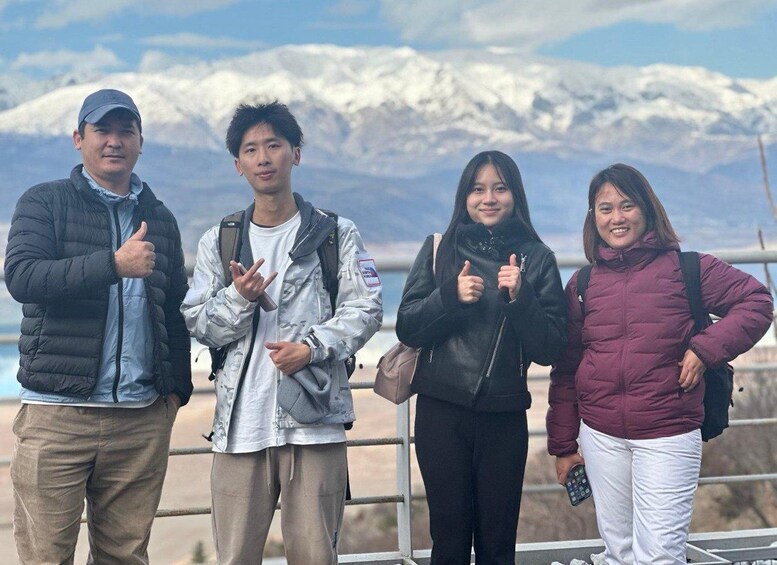 Four people standing on a viewing platform with snow-capped mountains in the background. 2