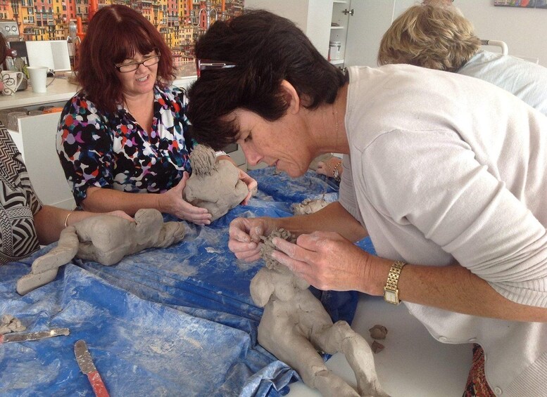People engaged in pottery making, with clay sculptures and tools on a table. 1