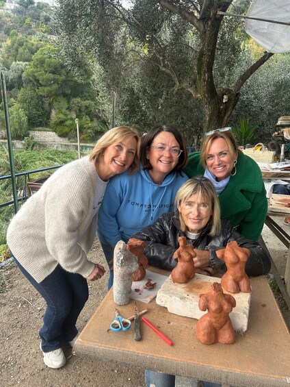 Three people posing with clay sculptures and tools on a table outdoors. 3